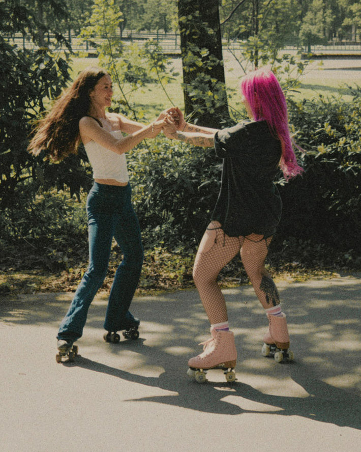 Two people wearing Rookie roller skates, skate in a park holding each others hands.